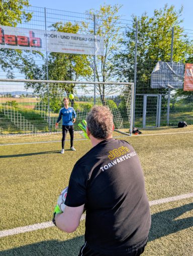 Zwei Personen auf einem Fußballfeld, einer bereit zum Schuss, der andere im Tor.