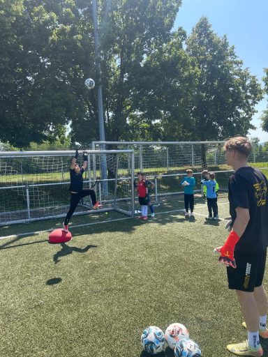 Ein Torwart trainiert mit mehreren Kindern auf einem Fußballplatz.
