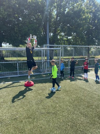 Ein Trainer steht auf einem Ball, während Kinder beim Fußballtraining zuschauen.