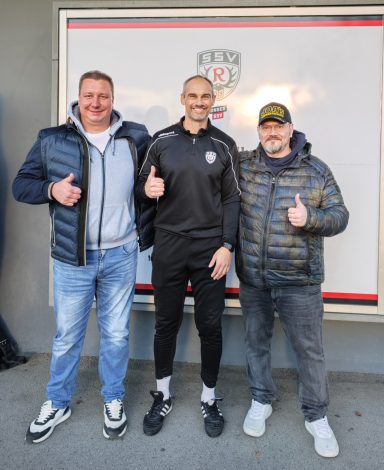 Drei Männer in sportlicher Kleidung zeigen Daumen nach oben vor einer Wand.