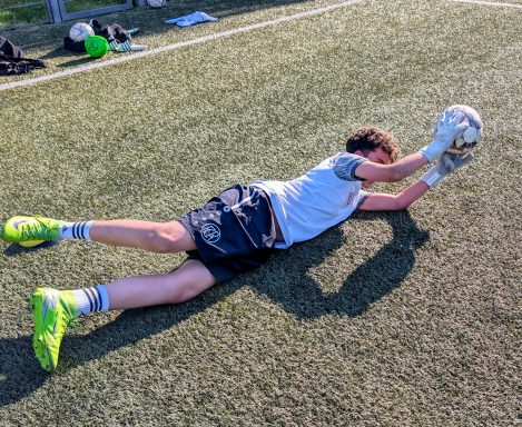 Torwart in Aktion, der einen Ball auf einem Fußballfeld fängt.