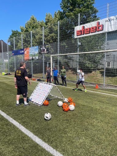Fußballtraining mit Torwartübungen und mehreren Spielern auf dem Platz.